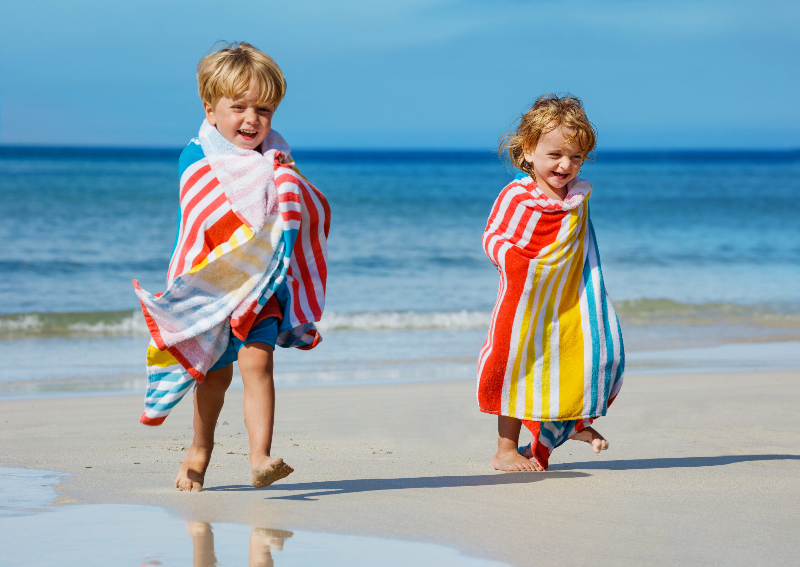 children boy, girl covered in towel run after swim on beach