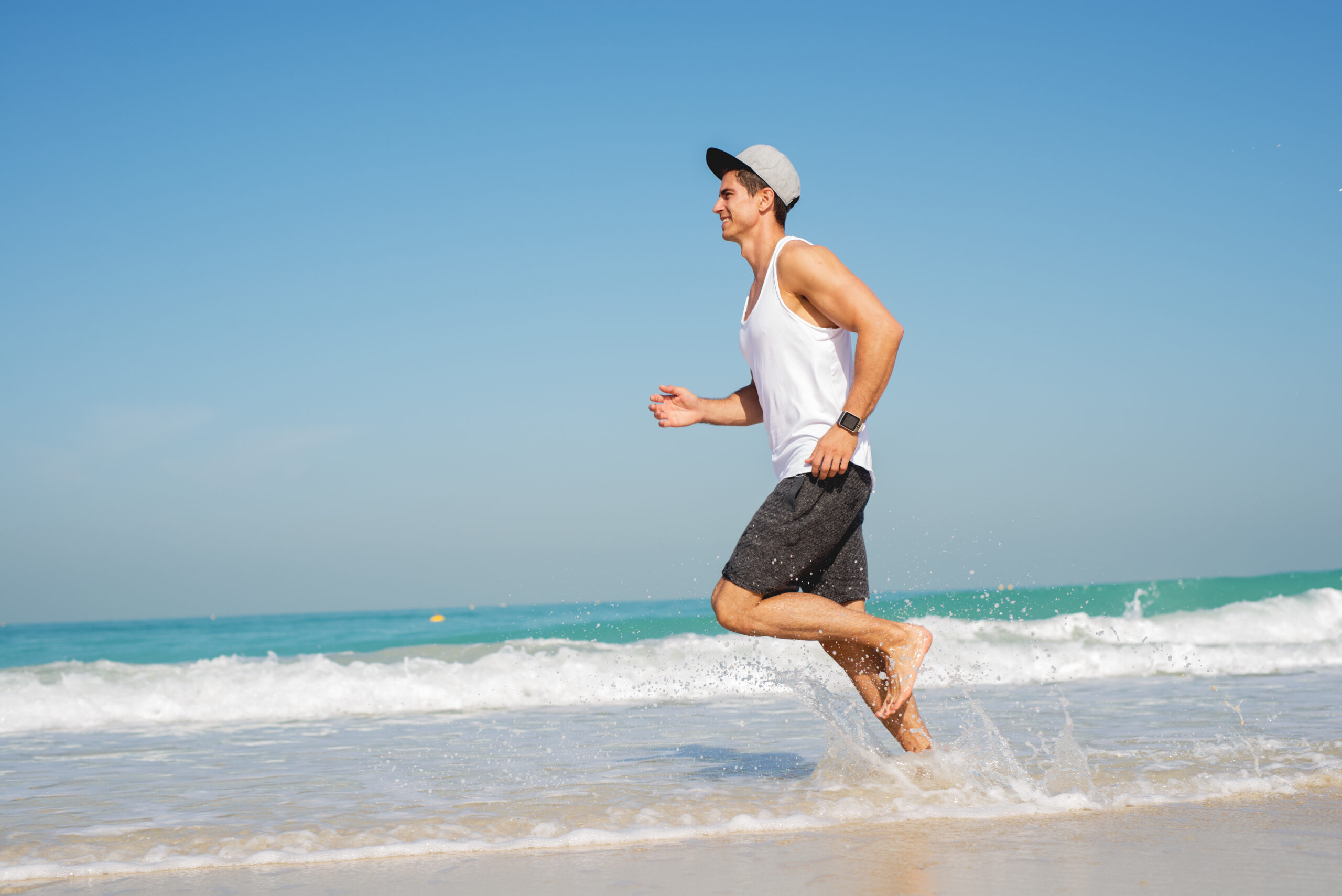 young sporty man running along beautiful beach, looking happy.